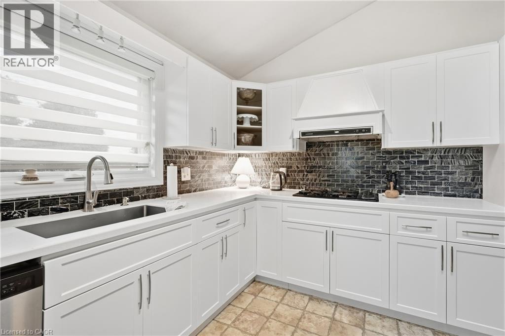 White shaker cabinetry, dark subway tile backsplash, white countertops, stainless steel sink with gooseneck faucet, and a built-in cooktop with range hood - 76 Madeira Crescent, Cambridge, ON