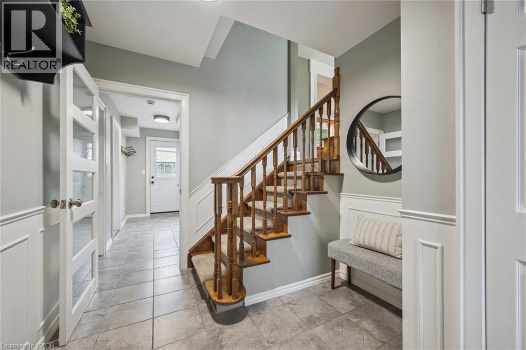 Tiled flooring, wood staircase with carpet runner, wainscoting, and a white paneled door with frosted glass inserts - 112 Margaret Avenue N, Waterloo, ON