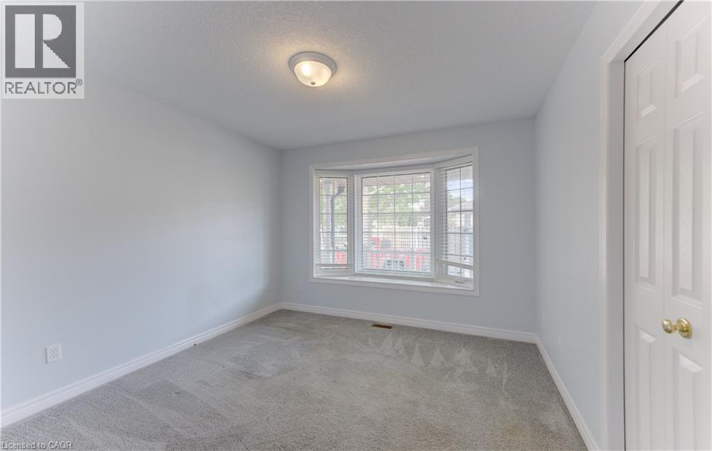 2nd Main Floor Bedroom featuring bay window with blinds, light gray wall paint, gray carpeting, white trim, and a ceiling-mounted light fixture and closet. - 25 Bankside Drive Unit# 2, Kitchener, ON