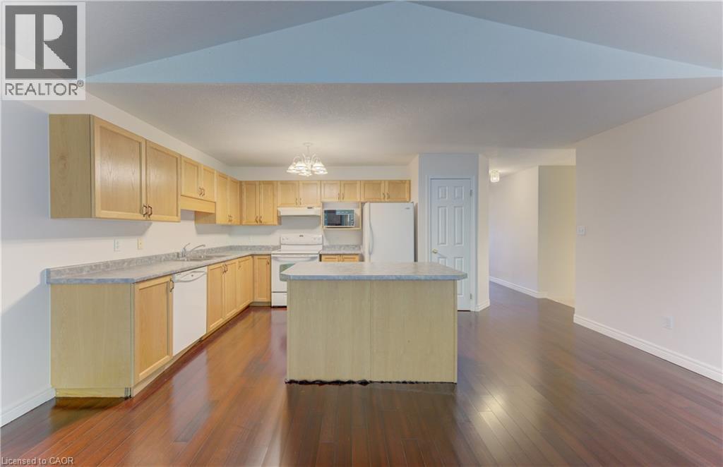 Kitchen featuring wood-finish cabinetry, light-toned countertops, and a central island - 25 Bankside Drive Unit# 2, Kitchener, ON
