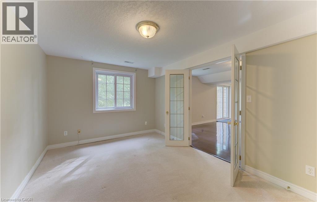 Carpeted room with a double-paned window, flush-mount ceiling light, and French doors featuring glass panels - 25 Bankside Drive Unit# 2, Kitchener, ON