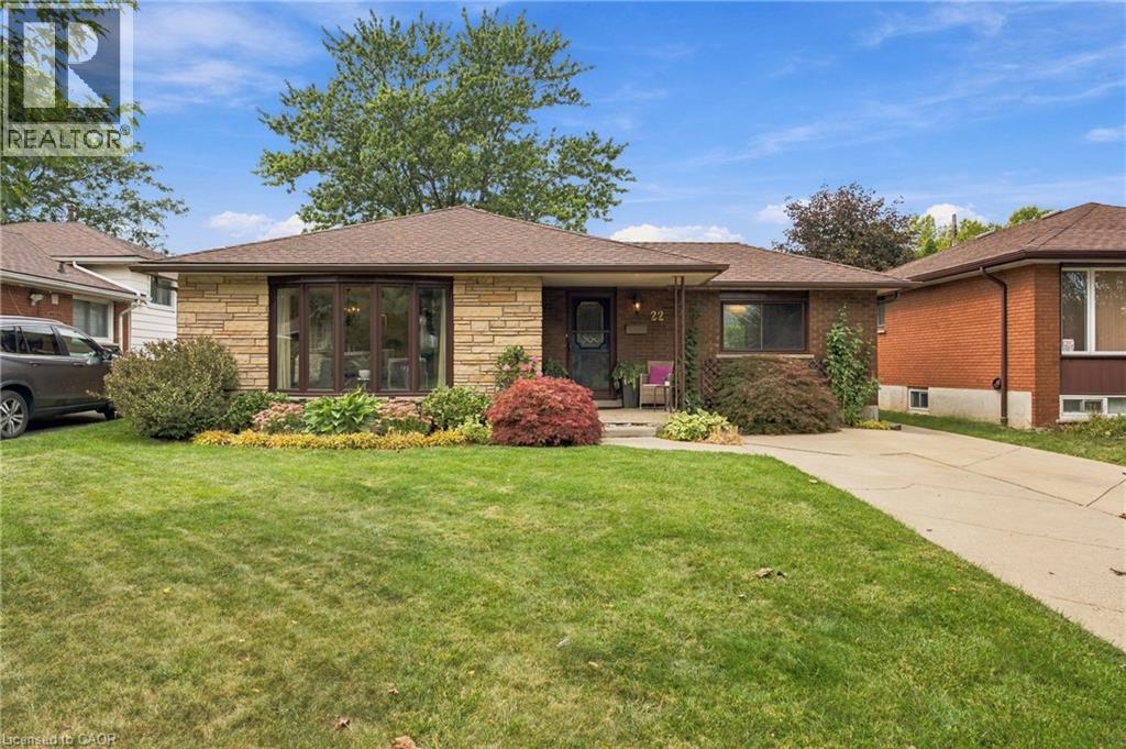 Brick and stone facade, front yard with mature landscaping, pitched shingle roof, paved driveway, and covered entry - 22 Sycamore Street, Hamilton, ON