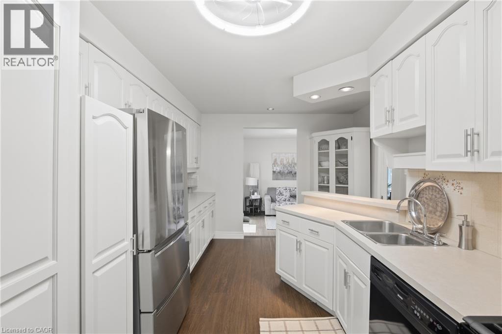 White cabinetry with arched upper panels, stainless steel refrigerator, dual basin stainless steel sink, black built-in dishwasher, and wood-finish flooring - 22 Sycamore Street, Hamilton, ON