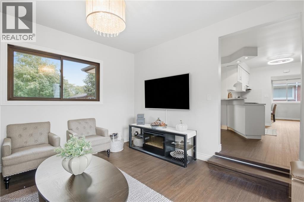 Wood-finish flooring throughout, with a large window and a contemporary chandelier - 22 Sycamore Street, Hamilton, ON