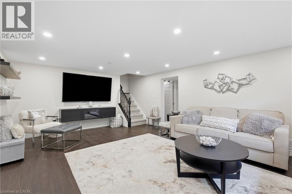 Recessed ceiling lighting, wood-finish flooring, staircase with dark wood railing, neutral wall color, and a built-in media console - 22 Sycamore Street, Hamilton, ON