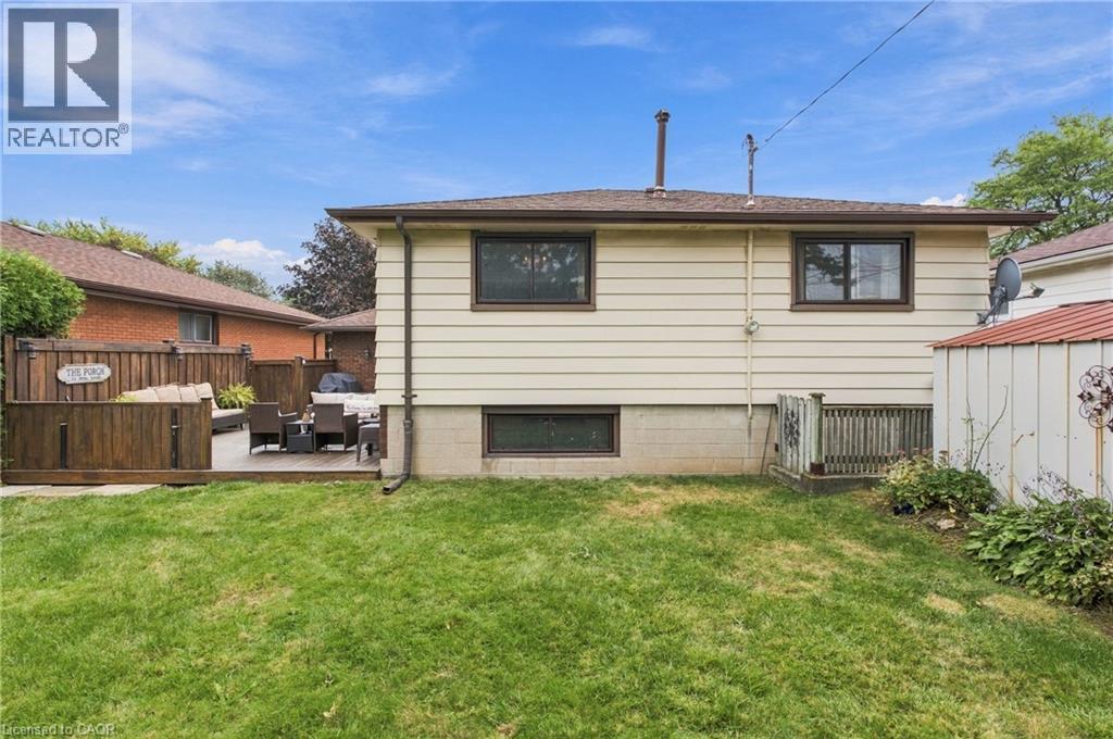 Expansive backyard featuring a wood deck, wood privacy fencing, and a manicured lawn - 22 Sycamore Street, Hamilton, ON