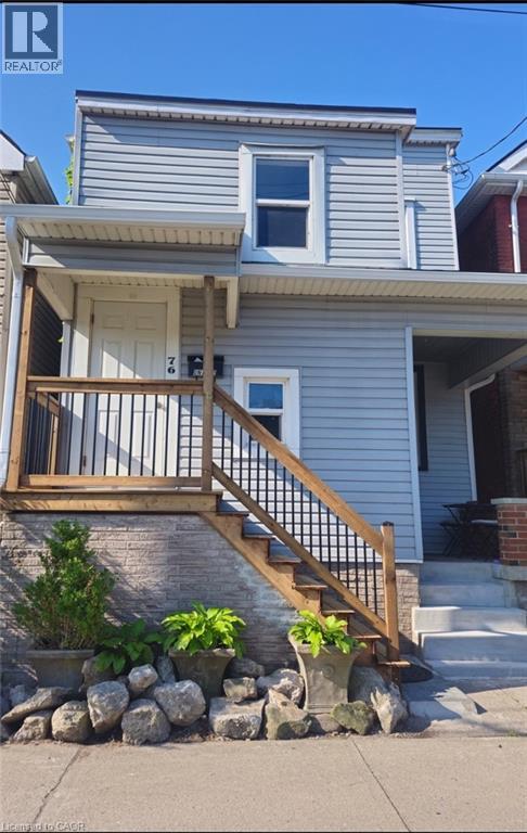 Light blue siding exterior with a covered porch featuring wooden railings and black balusters - 76 Burlington Street E, Hamilton, ON