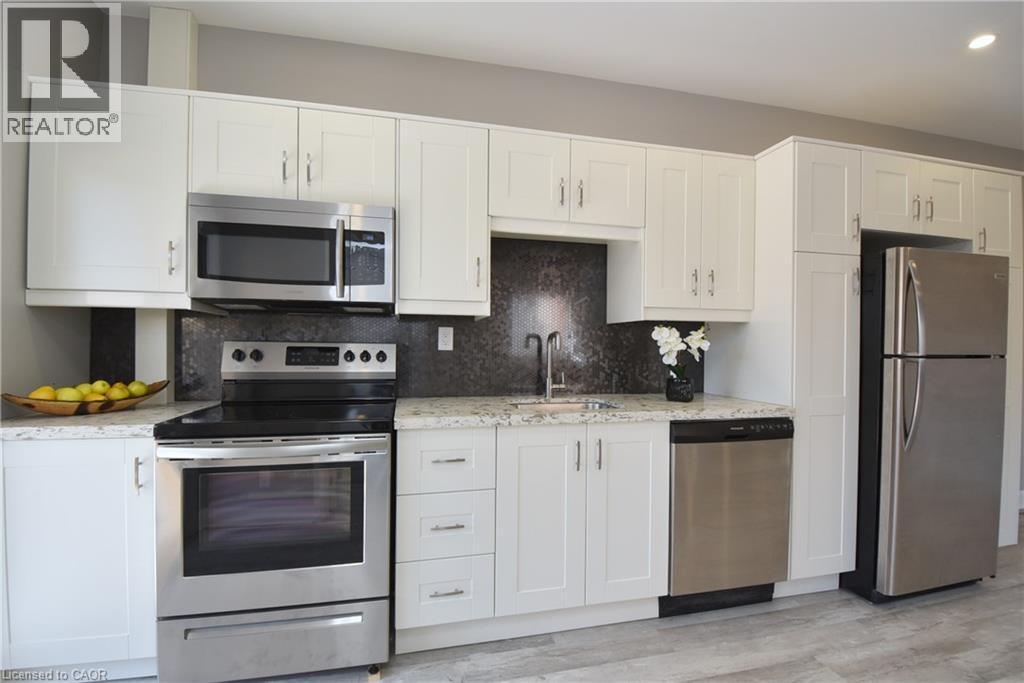 White shaker-style cabinetry with stainless steel hardware, stainless steel appliances, speckled stone countertops, and a dark textured backsplash - 76 Burlington Street E, Hamilton, ON