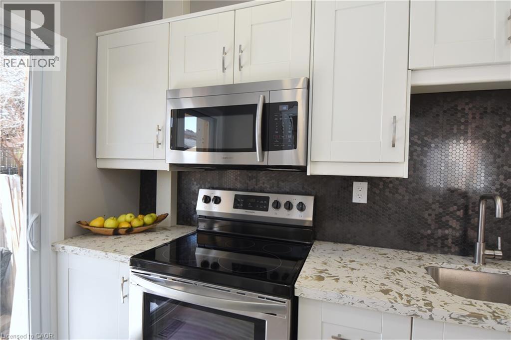 White shaker-style cabinetry, stainless steel microwave, black ceramic cooktop range, dark penny tile backsplash, and light-toned countertops - 76 Burlington Street E, Hamilton, ON