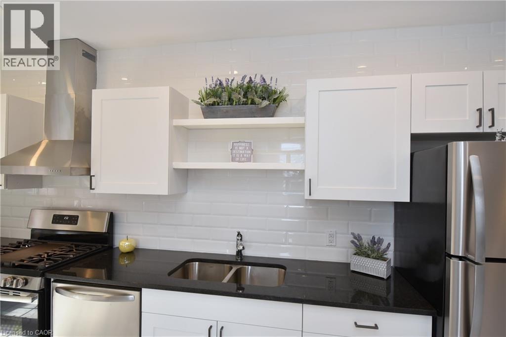 Modern kitchen featuring white shaker-style cabinetry, dark countertops, white subway tile backsplash, and stainless steel appliances - 76 Burlington Street E, Hamilton, ON