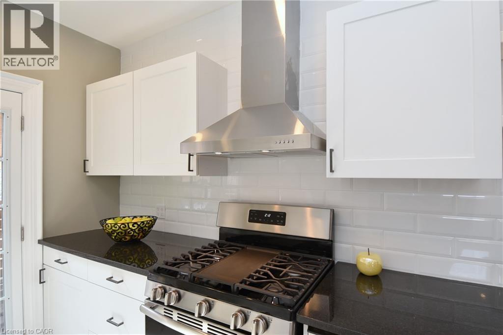 Kitchen featuring white shaker-style cabinetry, dark countertops, a subway tile backsplash, a stainless steel range, and a stainless steel hood vent - 76 Burlington Street E, Hamilton, ON