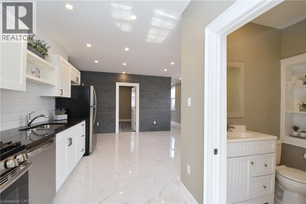 Kitchenette featuring white shaker cabinetry, dark countertops, a stainless steel sink, and a stainless steel range - 76 Burlington Street E, Hamilton, ON