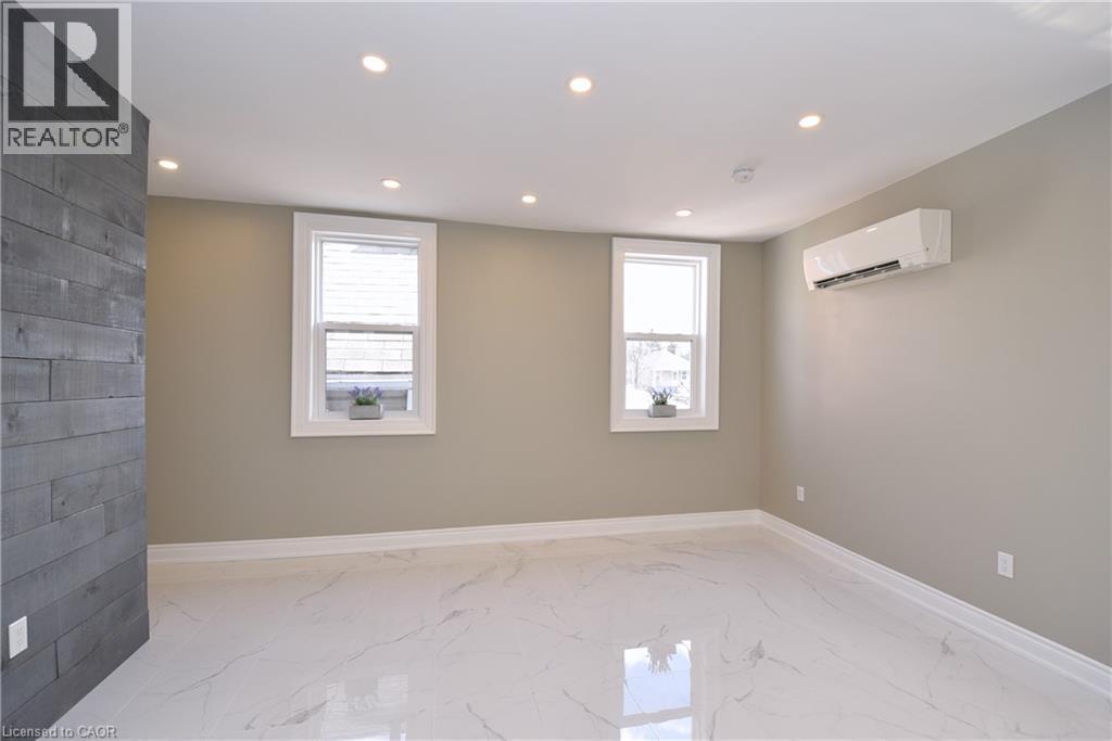 Recessed lighting, wood-finish accent wall, white trim, two windows, and wall-mounted climate control unit - 76 Burlington Street E, Hamilton, ON