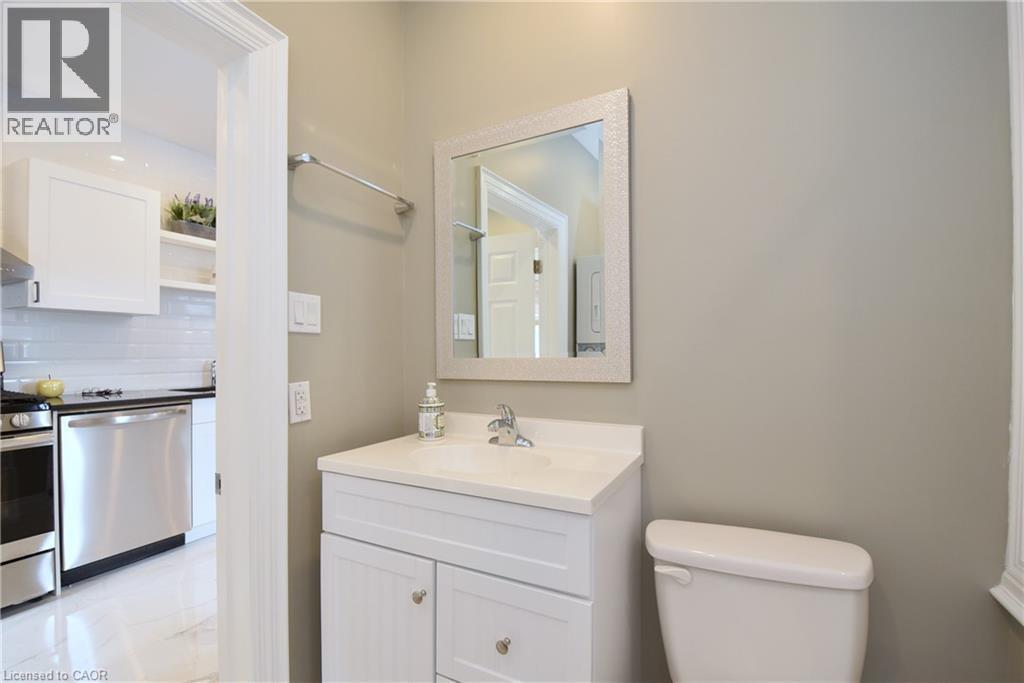 White vanity with a single basin sink, framed mirror, and chrome faucet - 76 Burlington Street E, Hamilton, ON