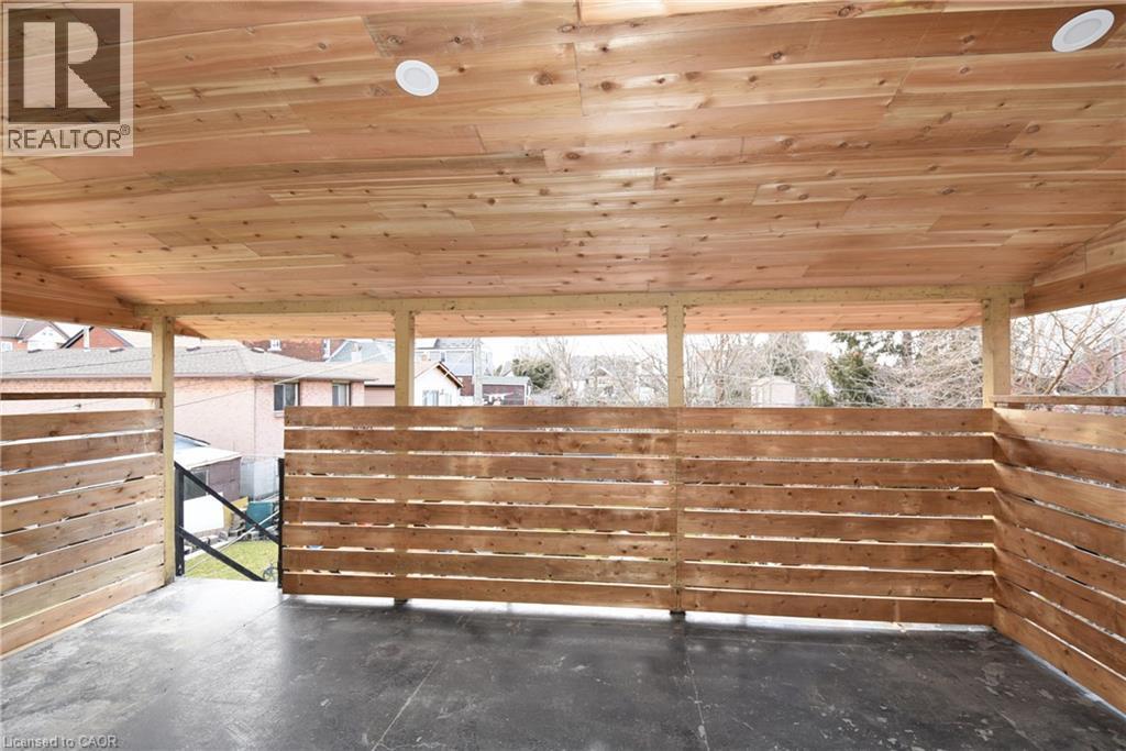 Covered outdoor area featuring a wood plank ceiling with recessed lighting, wood slat fencing, and a dark-toned flooring surface - 76 Burlington Street E, Hamilton, ON