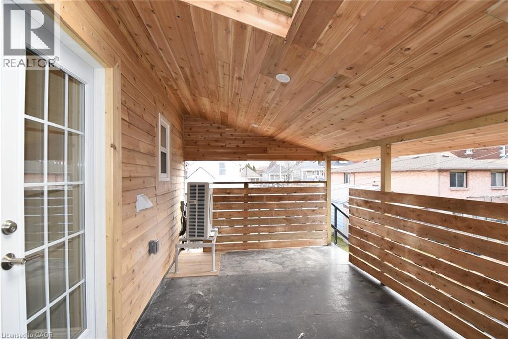 Covered outdoor patio featuring wood-finish ceiling, wood-finish siding, wood-slat privacy walls, and a glass-paneled exterior door - 76 Burlington Street E, Hamilton, ON