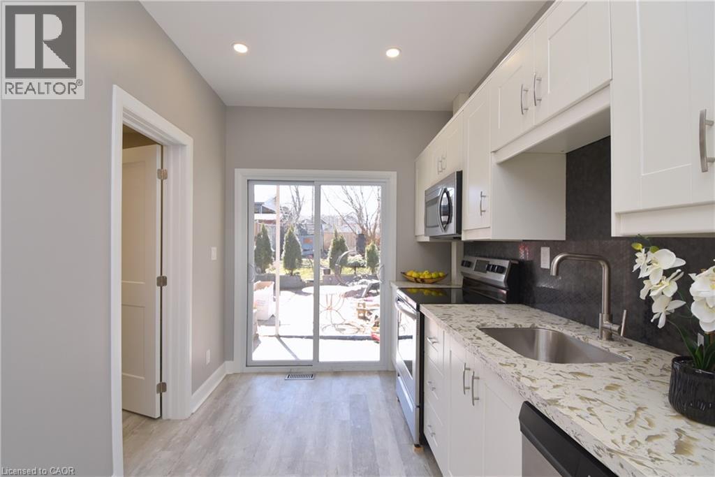 Kitchen featuring white cabinetry, light-toned countertops, a stainless steel sink, and wood-finish flooring - 76 Burlington Street E, Hamilton, ON