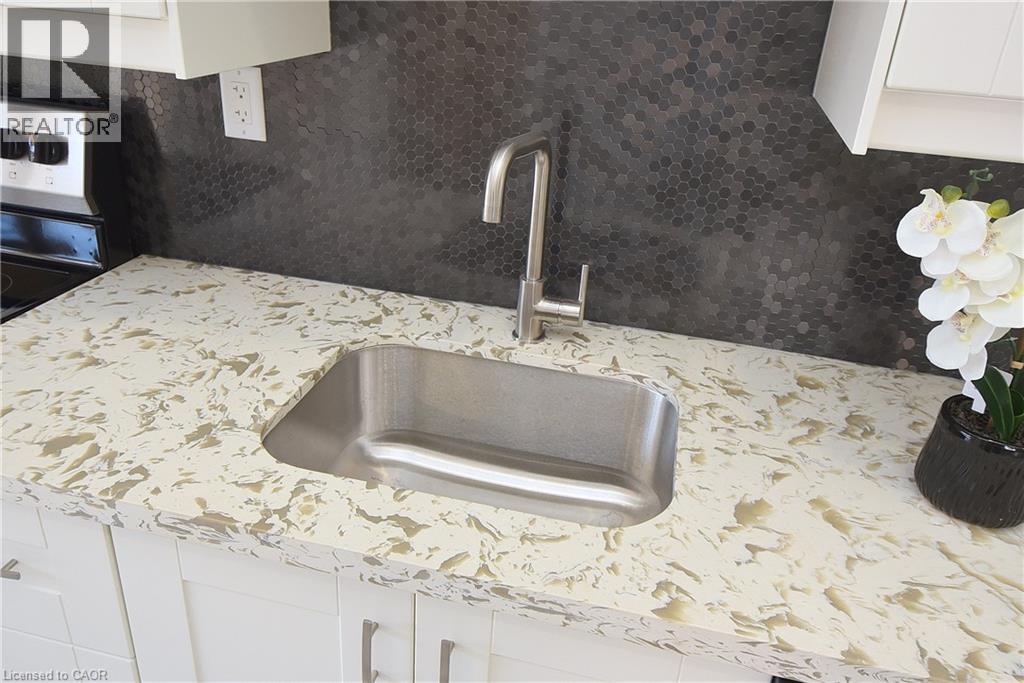 White shaker cabinetry with brushed nickel hardware, light-toned countertop, stainless steel undermount sink, gooseneck faucet, and hexagonal tile backsplash - 76 Burlington Street E, Hamilton, ON