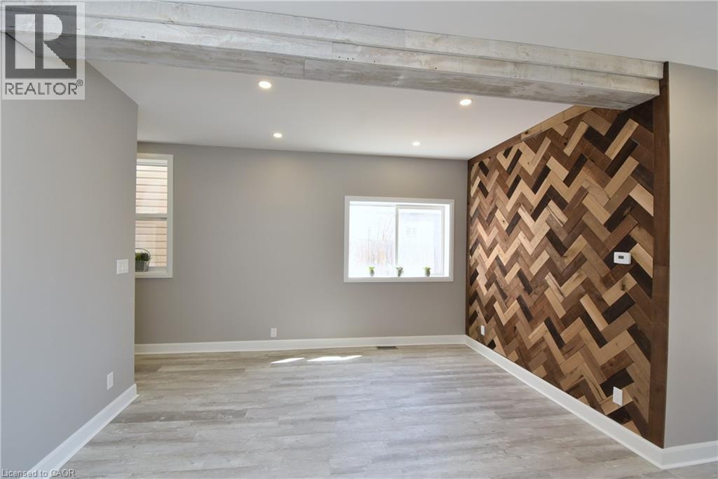 Reclaimed wood accent wall with a herringbone pattern, light wood-finish flooring, recessed ceiling lighting, and a prominent exposed beam - 76 Burlington Street E, Hamilton, ON