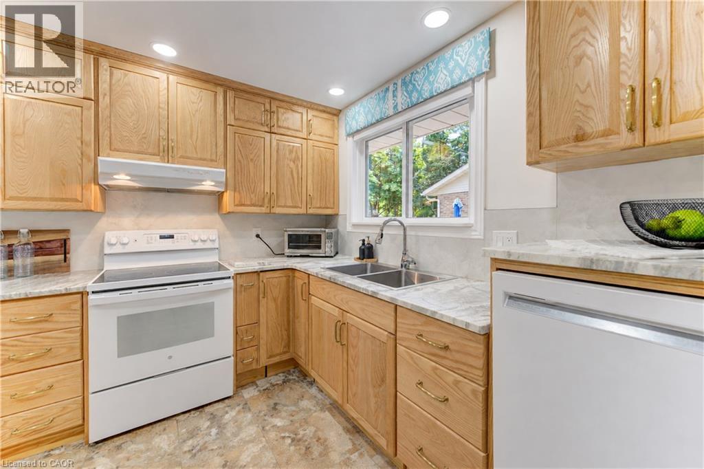 Wood-finish cabinetry, light-toned countertops, tile backsplash, white appliances, and a double basin sink - 422 Grangewood Drive, Waterloo, ON
