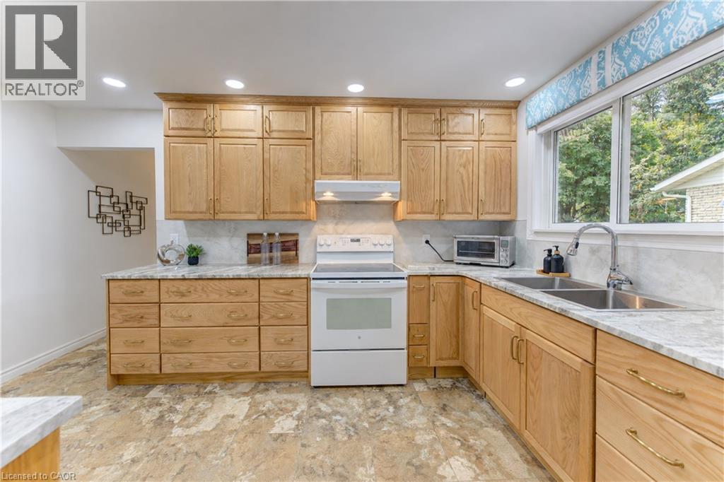 Kitchen featuring light wood cabinetry, stone countertops, a double basin stainless steel sink with a gooseneck faucet, a built-in range, and recessed lighting - 422 Grangewood Drive, Waterloo, ON