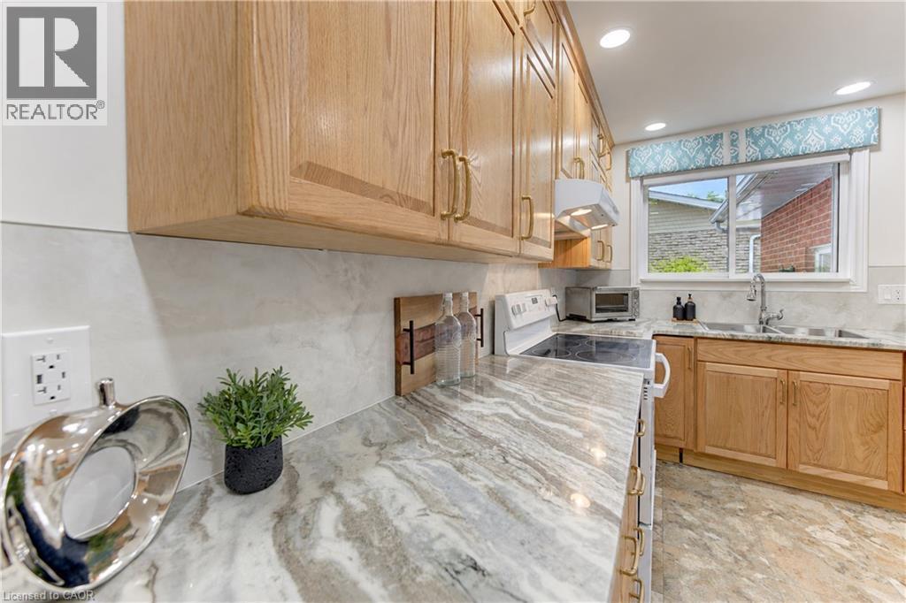 Wood-finish cabinetry with brass hardware, patterned countertops, a white electric range, and a stainless steel sink with a chrome faucet - 422 Grangewood Drive, Waterloo, ON