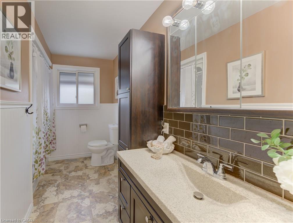 Vanity with integrated sink and chrome faucet, dark subway tile backsplash, medicine cabinet with integrated lighting, wood-finish storage cabinet, and window with privacy glass - 422 Grangewood Drive, Waterloo, ON