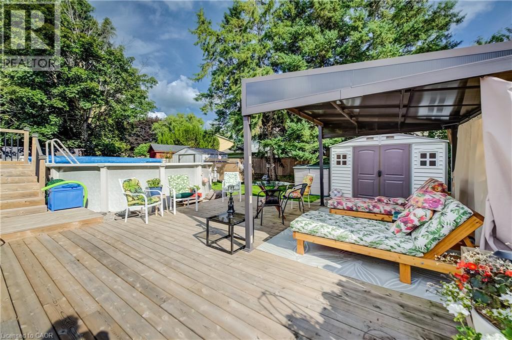 Expansive wood-finish deck featuring an above-ground pool with stairs, a covered patio area, and a storage shed - 422 Grangewood Drive, Waterloo, ON