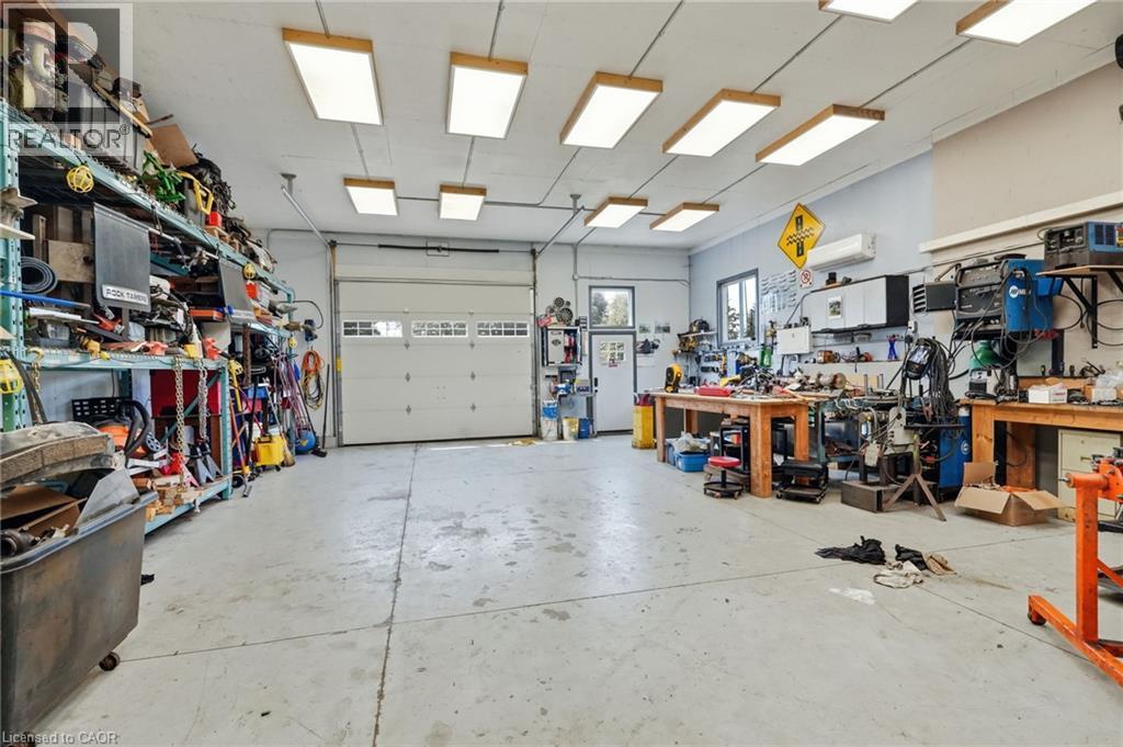 Spacious workshop with a large overhead door, multiple fluorescent ceiling fixtures, and expansive concrete flooring - 1311 W Concession 6 Road, Flamborough, ON