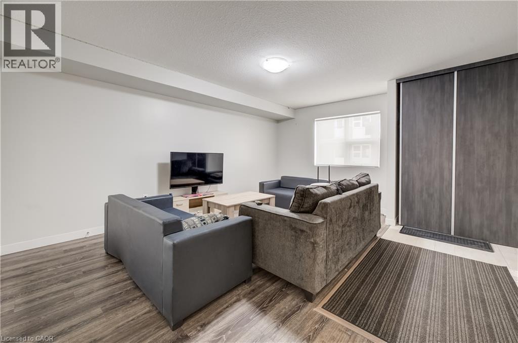 Wood-finish flooring throughout, bright white walls, and a window with roller shade - 338 Albert Street Unit# 114, Waterloo, ON