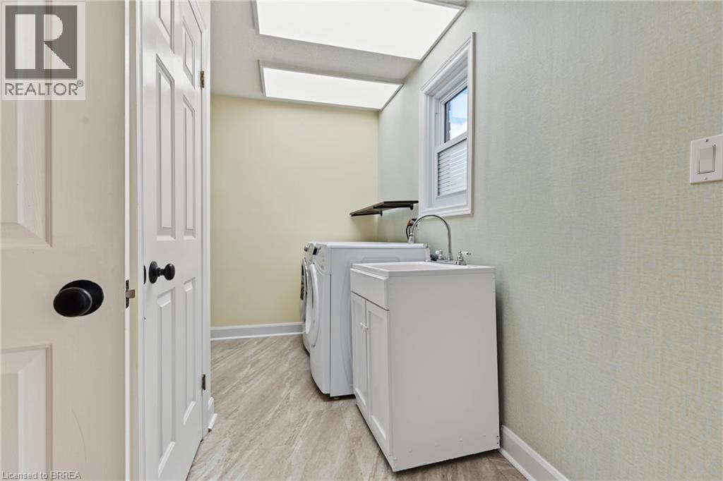 Laundry area featuring a utility sink with a white cabinet, wood-finish flooring, and a window with blinds - 141 Race Street, Paris, ON