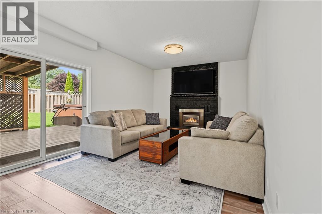 Bright interior with wood-finish flooring, a contemporary fireplace with a black brick surround, and a glass sliding door opening to an exterior wood deck - 141 Race Street, Paris, ON