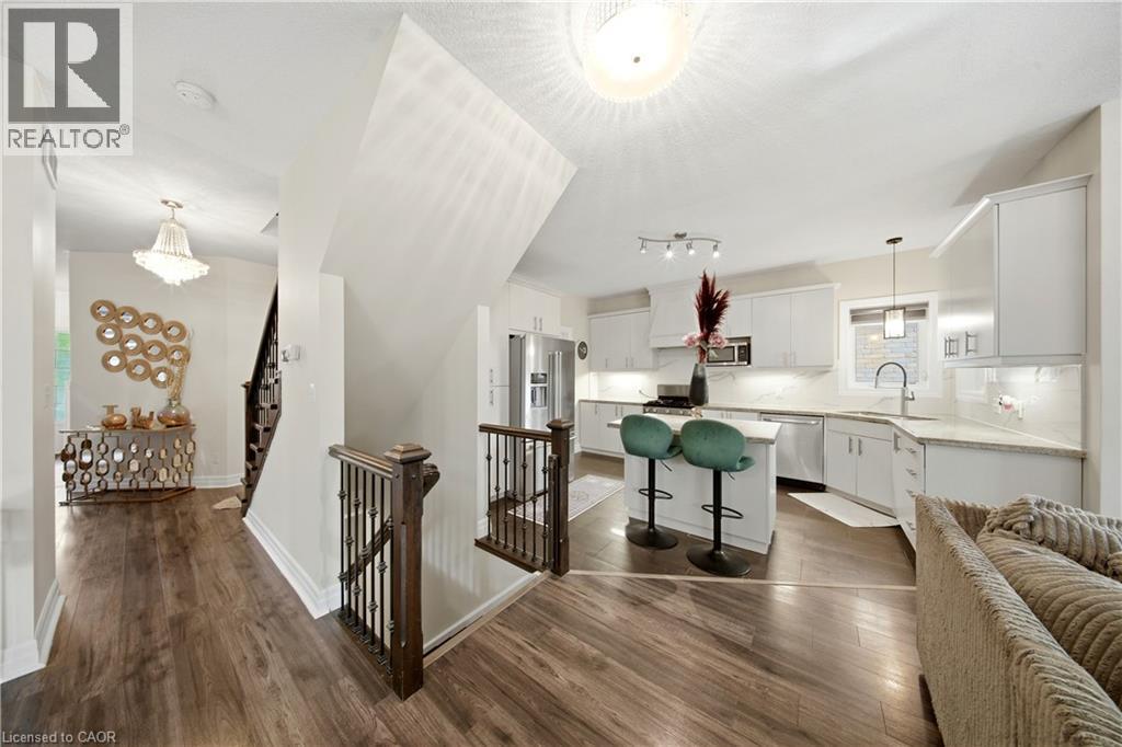 Open concept layout featuring wood-finish flooring, a contemporary kitchen with white cabinetry, stainless steel appliances, and a central island with seating - 167 Broadoaks Drive, Cambridge, ON