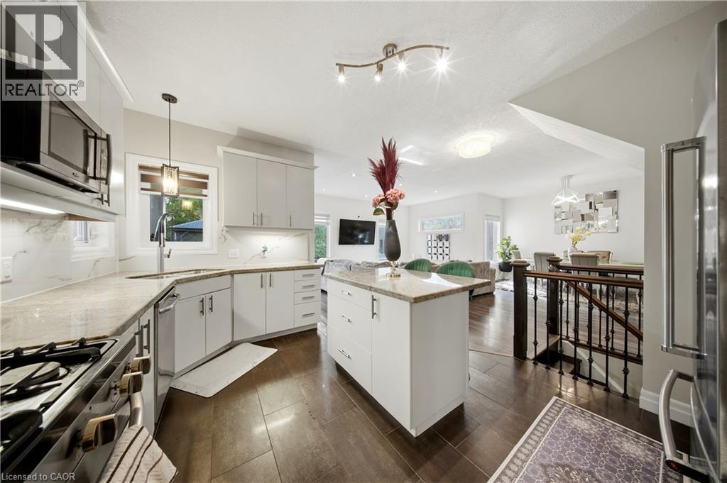 Kitchen featuring light cabinetry, a central island with a stone countertop, an integrated microwave, and a stainless steel oven - 167 Broadoaks Drive, Cambridge, ON