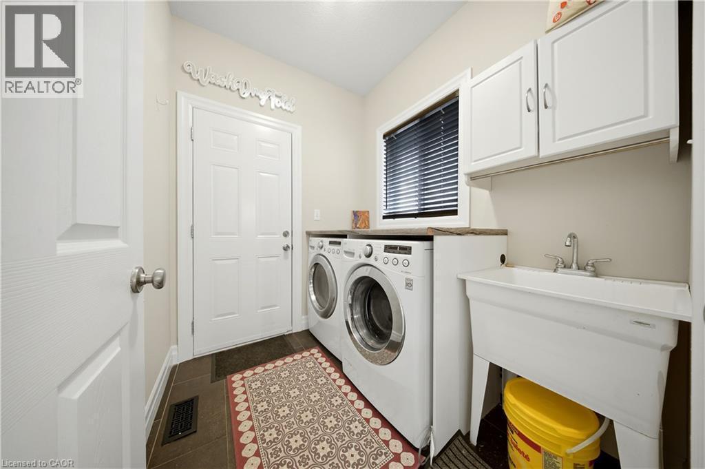 Functional utility room featuring dark tile flooring, white upper cabinetry, a window with blinds, and a built-in utility sink - 167 Broadoaks Drive, Cambridge, ON