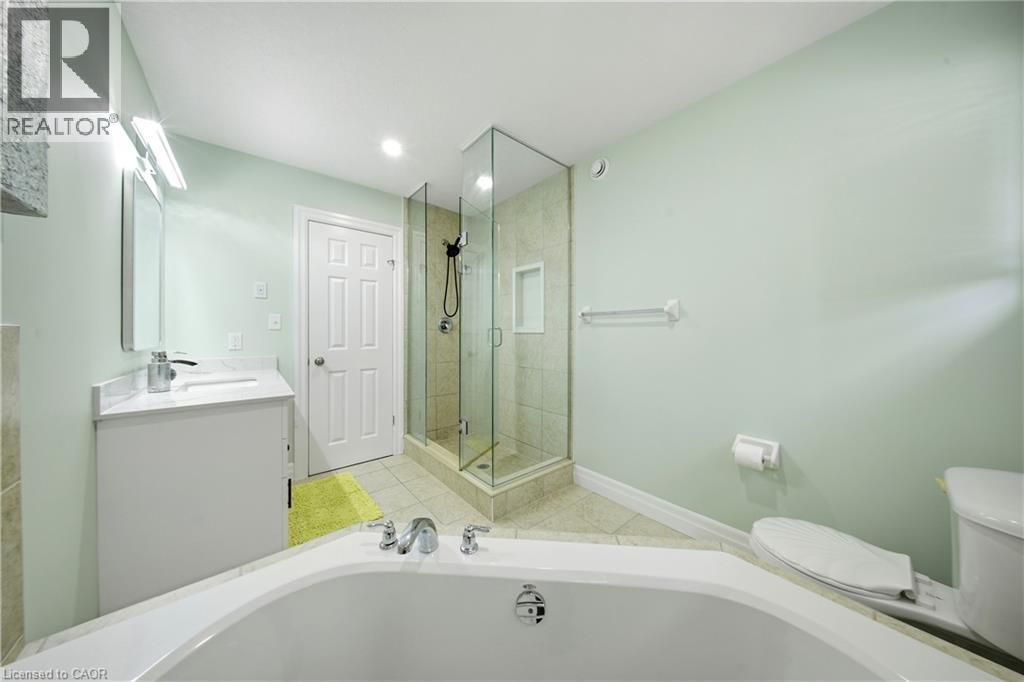 Corner soaking tub, glass-enclosed shower with tile surround, single vanity with integrated sink, tile flooring, and recessed lighting - 167 Broadoaks Drive, Cambridge, ON