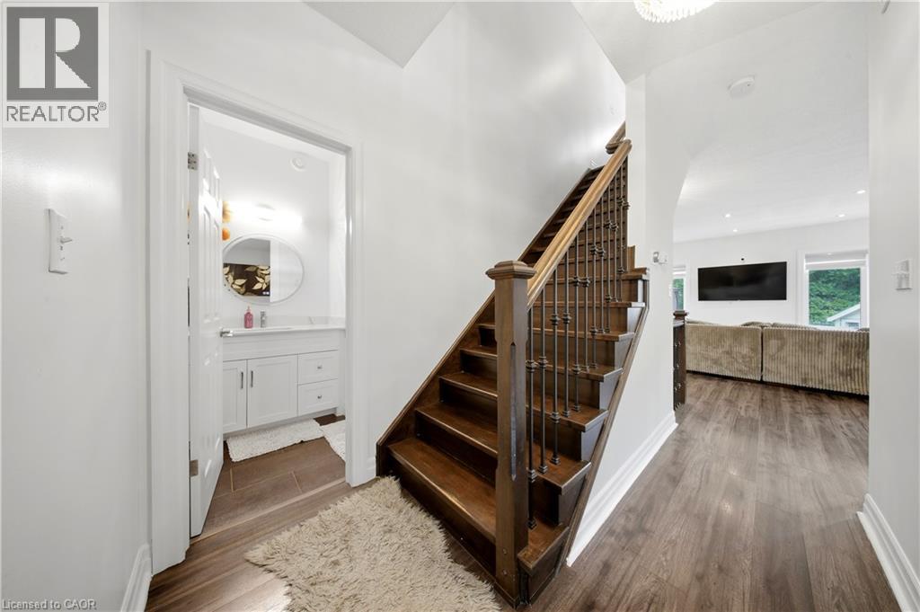Wood-finish flooring throughout, dark wood staircase with wrought iron balusters, white vanity with integrated sink, chrome faucet, and oval mirror, and recessed lighting - 167 Broadoaks Drive, Cambridge, ON