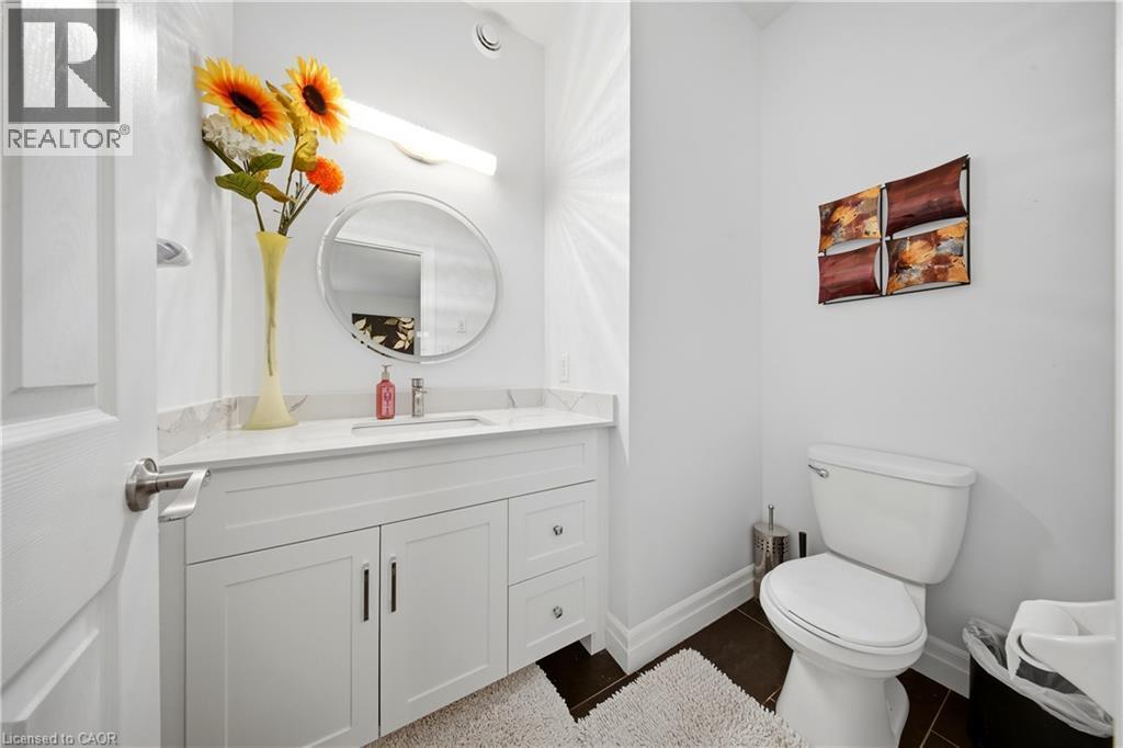 White vanity with integrated sink, stone countertop, matte black pulls, wall-mounted light fixture, and round mirror - 167 Broadoaks Drive, Cambridge, ON