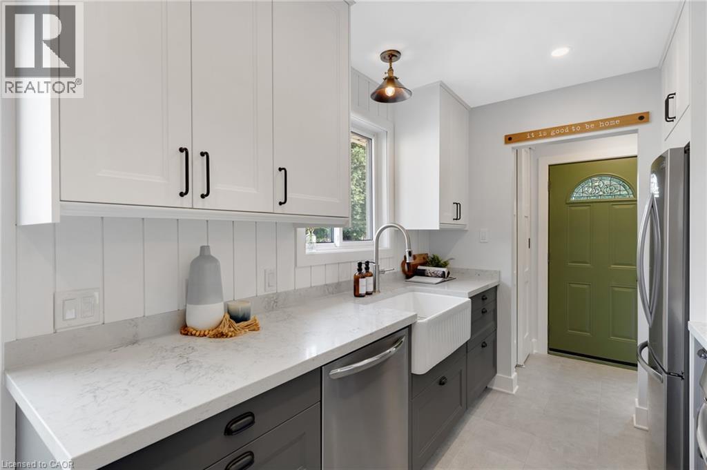 Kitchen featuring white upper cabinetry, dark lower cabinetry, light-toned countertops, a farmhouse sink with a gooseneck faucet, and a paneled backsplash - 477 Kingscourt Drive Unit# B, Waterloo, ON