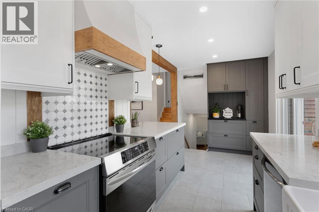 Gourmet kitchen featuring a stainless steel range, white shaker cabinetry, custom wood range hood, patterned tile backsplash, and light-colored countertops - 477 Kingscourt Drive Unit# B, Waterloo, ON