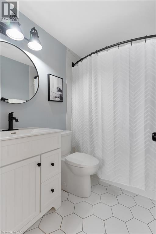 White hexagonal tile flooring, white vanity with black hardware, black faucet, circular mirror, and track lighting - 477 Kingscourt Drive Unit# B, Waterloo, ON