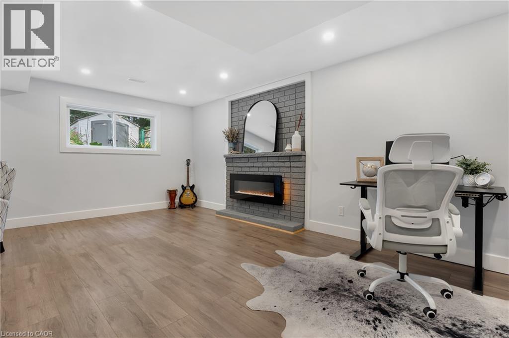 Recessed lighting, wood-finish flooring, brick-surround fireplace with hearth, and a window with white trim - 477 Kingscourt Drive Unit# B, Waterloo, ON