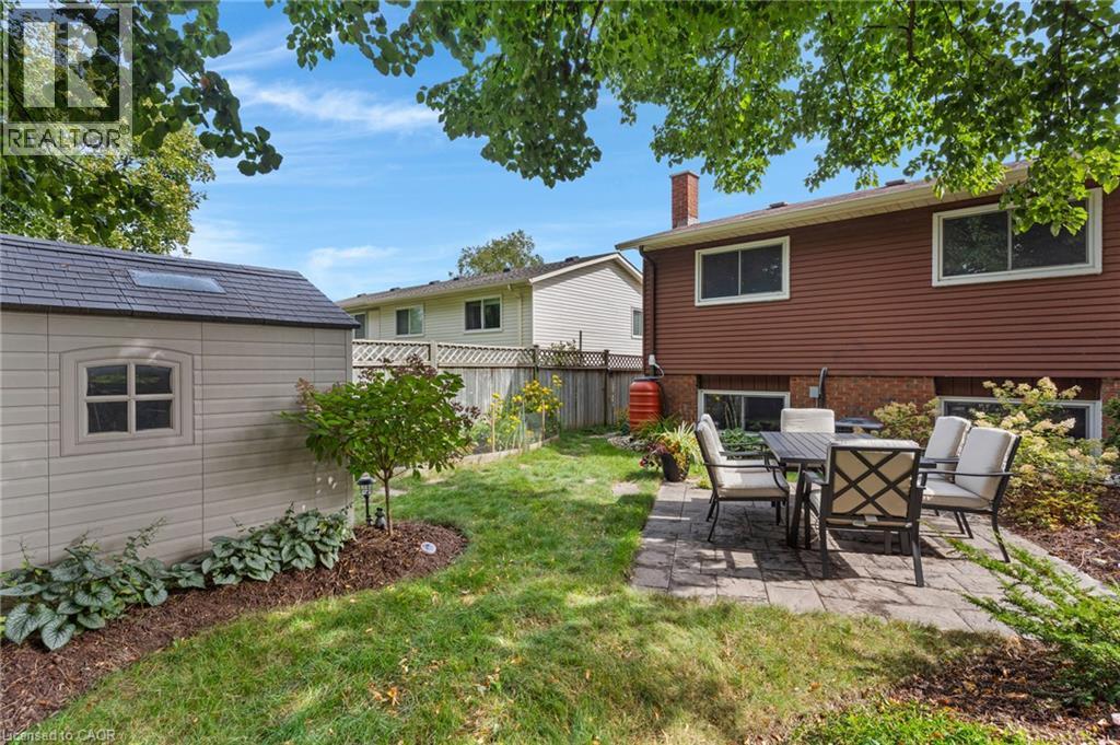 Spacious rear yard featuring a paved patio, mature trees, and a detached storage shed with a skylight - 477 Kingscourt Drive Unit# B, Waterloo, ON