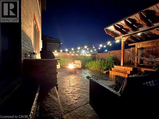 Expansive stamped concrete patio featuring a fire pit, string lighting, and a multi-level wooden deck with a covered pergola - 4073 Stadelbauer Drive, Beamsville, ON