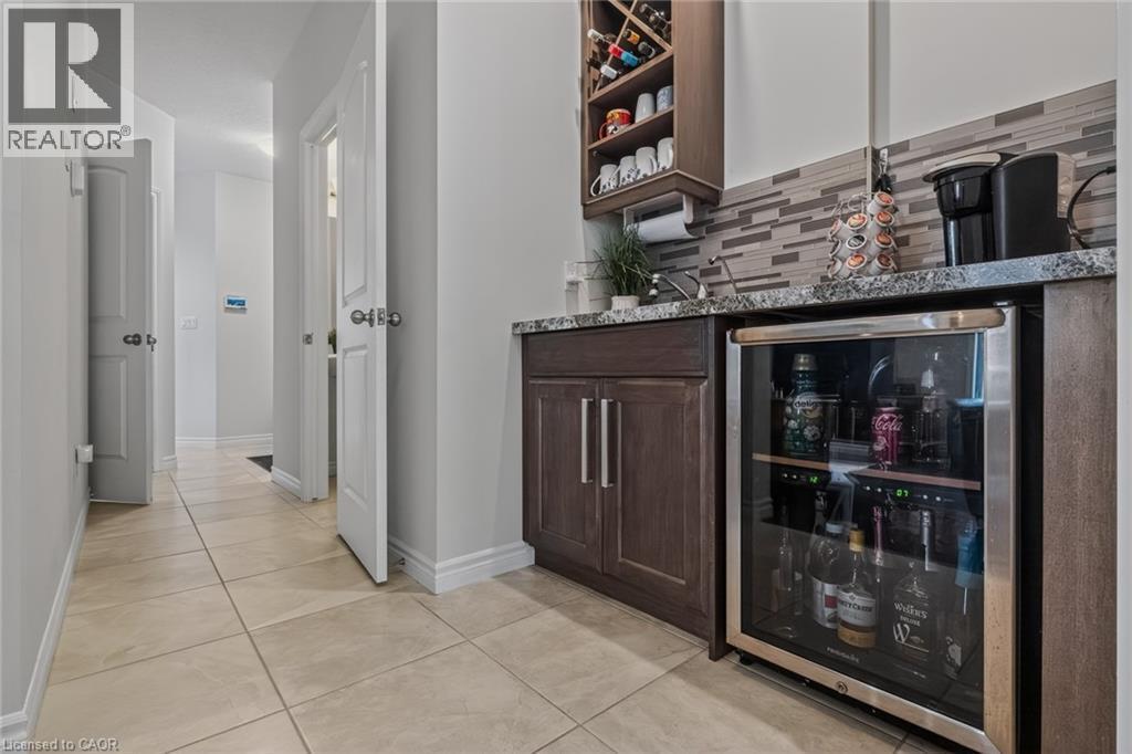 Built-in wet bar featuring dark wood-finish cabinetry, stone-finish countertop, under-mount sink, and a beverage refrigerator - 249 Woodway Trail, Simcoe, ON