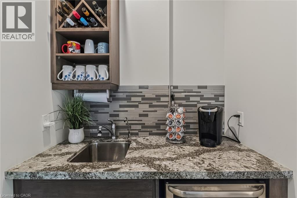 Wet bar featuring a stainless steel sink, patterned tile backsplash, granite-finish countertop, built-in wooden wine rack, and under-counter appliance - 249 Woodway Trail, Simcoe, ON