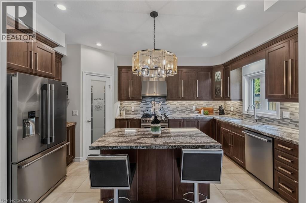 Kitchen featuring a central island with a granite countertop, dark wood-finish cabinetry, stainless steel appliances, tile flooring, and a decorative pendant light fixture - 249 Woodway Trail, Simcoe, ON