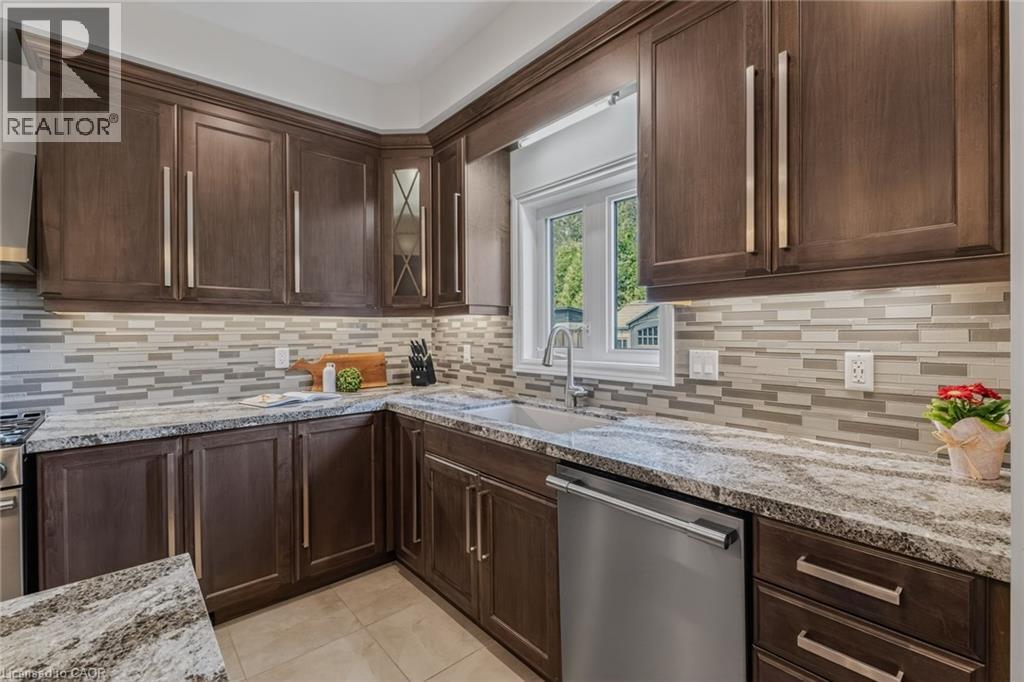 Kitchen featuring dark wood-finish cabinetry, light stone countertops, a mosaic tile backsplash, and stainless steel appliances - 249 Woodway Trail, Simcoe, ON