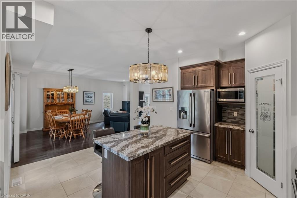 Kitchen featuring a central island with a granite countertop, dark wood-finish cabinetry, stainless steel appliances, and tile flooring - 249 Woodway Trail, Simcoe, ON
