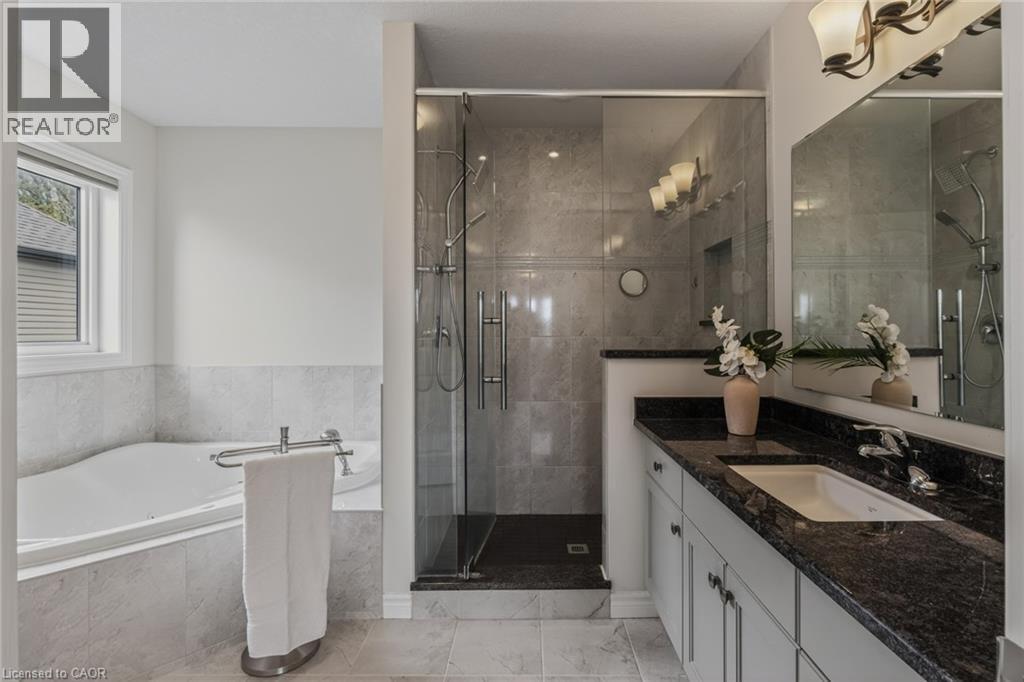 Bathroom featuring a glass-enclosed shower, a built-in soaking tub, a double vanity with dark stone countertops, and tile flooring - 249 Woodway Trail, Simcoe, ON